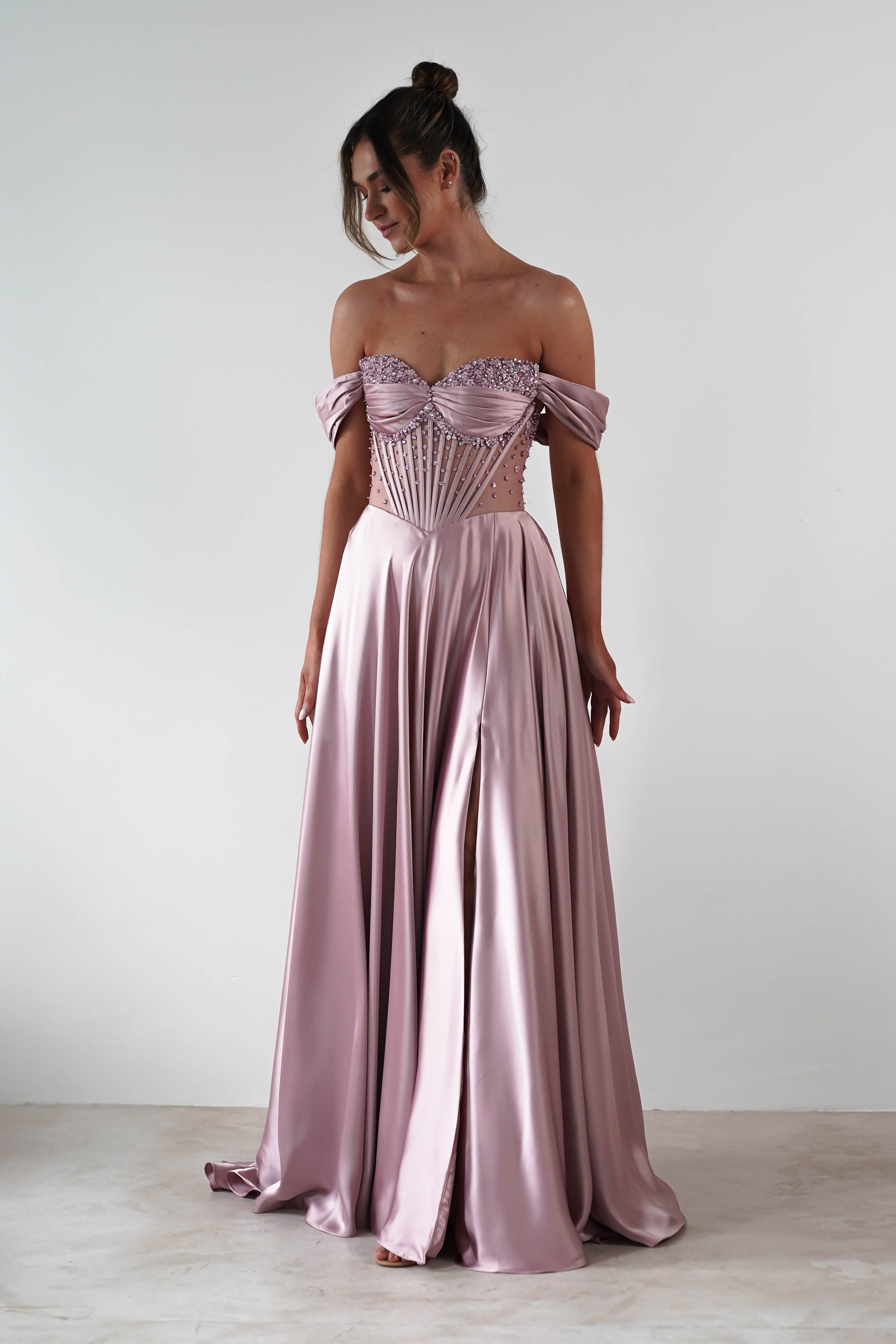 A woman wears a shiny lavender A-Line gown with a strapless sweetheart neckline and fitted corset-style bodice. The floor-length satin skirt flows elegantly as she stands against a plain white background.