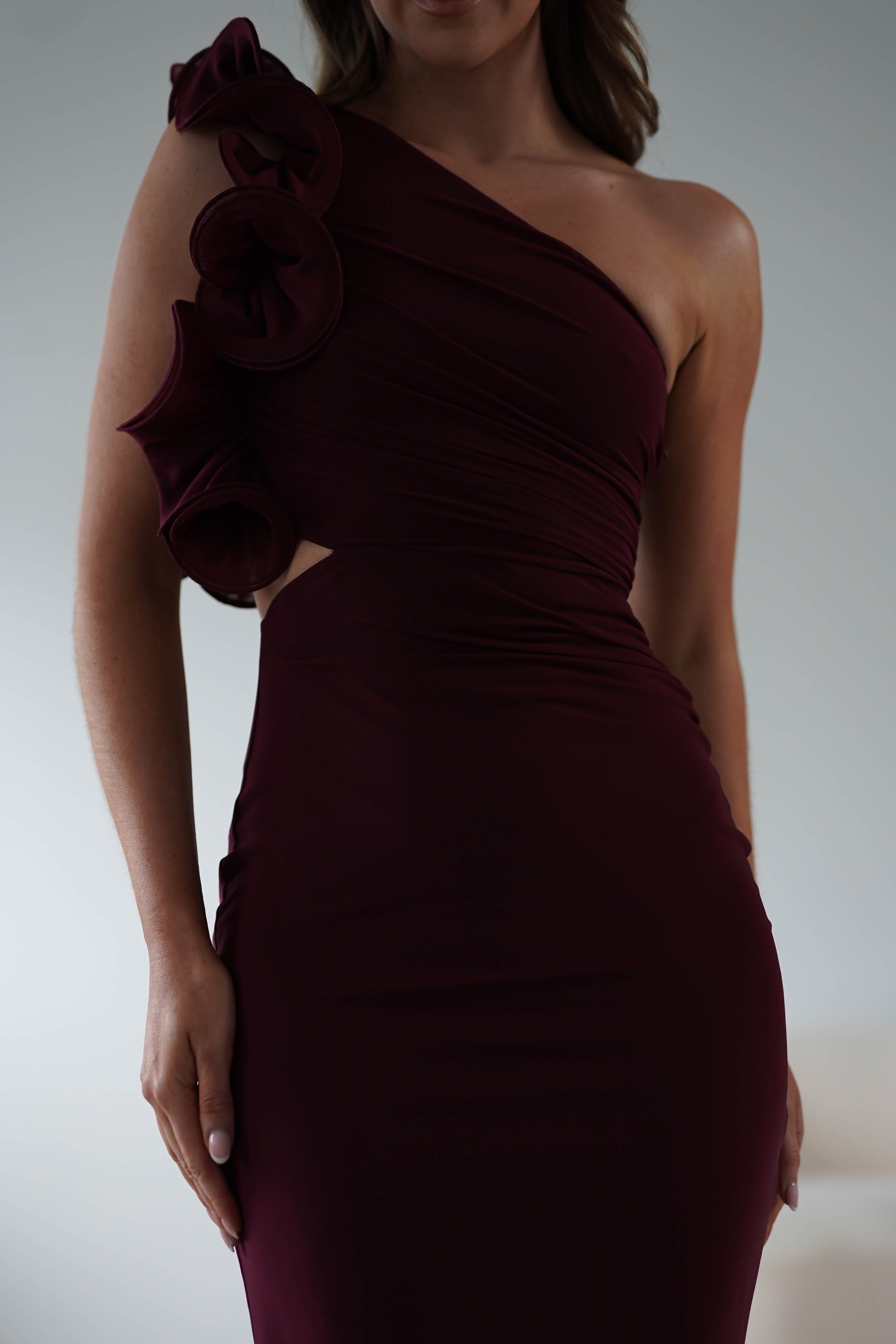 A woman wearing a dark burgundy Midaxi dress with ruffle details and the kind of wear-all-day comfort you crave. The form-fitting design is elegantly draped, and the neutral background perfectly emphasizes the stylish outfit.