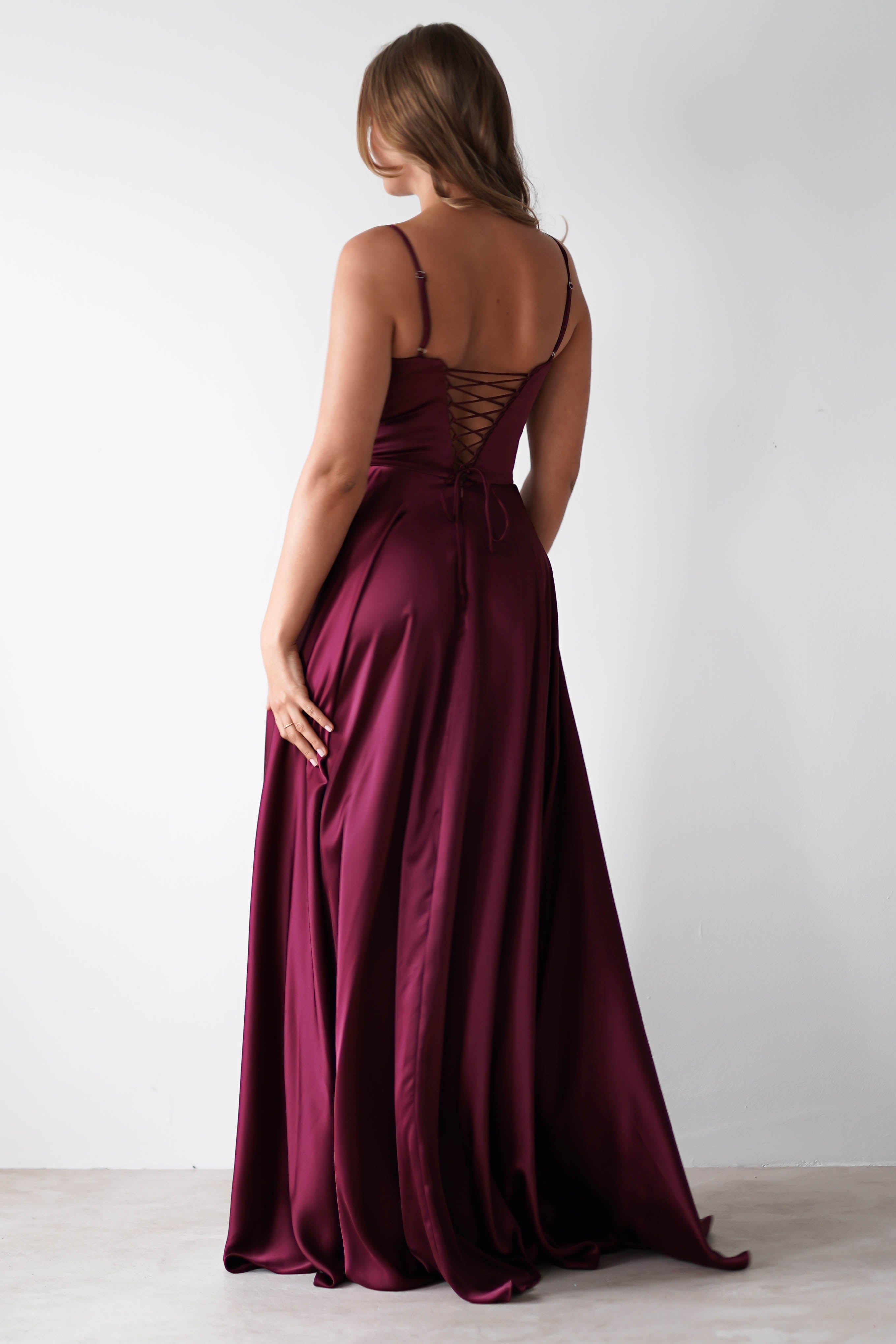 A woman stands facing away, wearing a floor-length satin gown with a lace-up back—perfect for formal events. Her hair is loose as she poses against a plain white background.