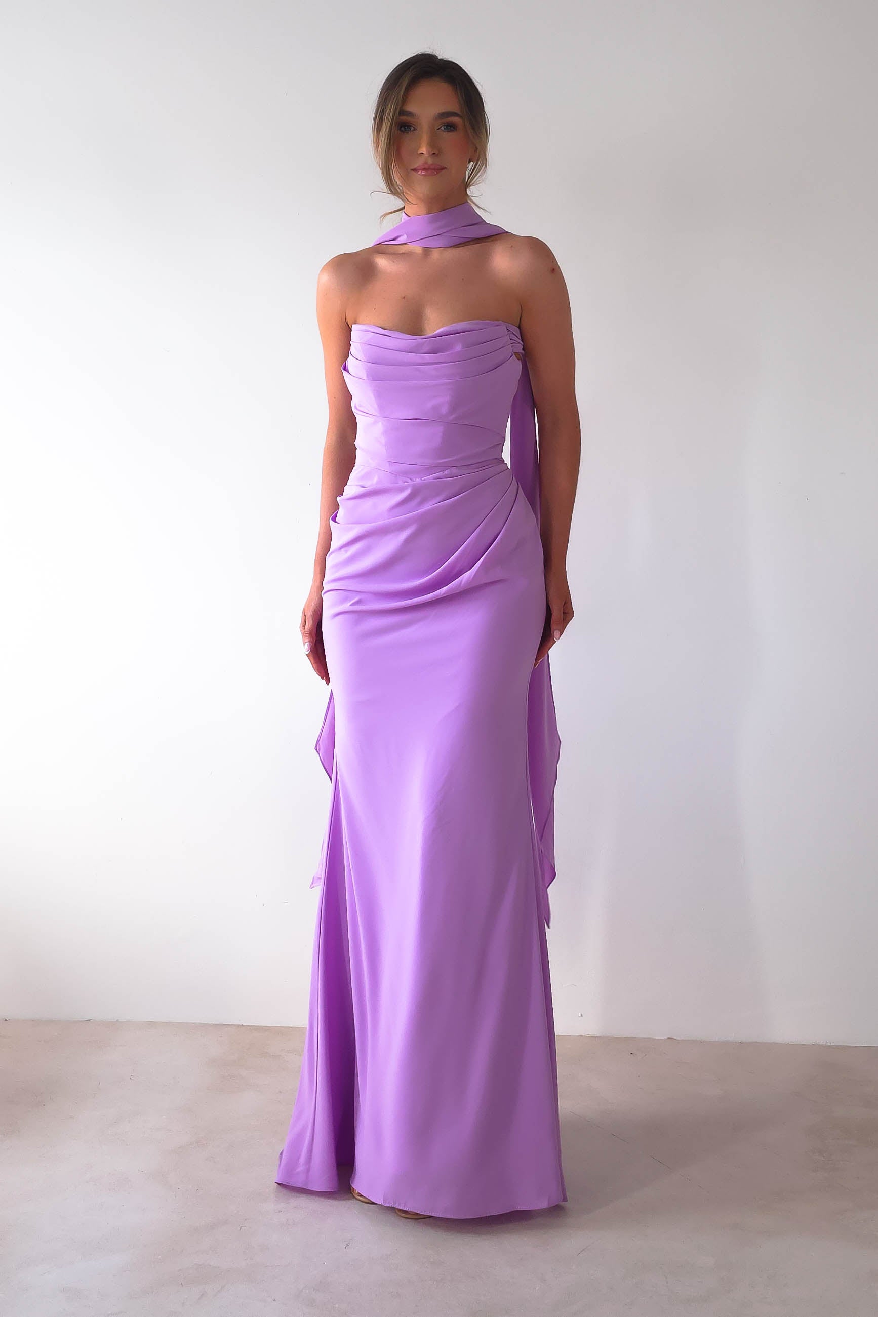 A person in a strapless lavender Lisa Multiway Chiffon Gown with a matching choker stands against a plain white background. The dress features elegant draping, versatile ties, and a fitted silhouette that embodies timeless sophistication.