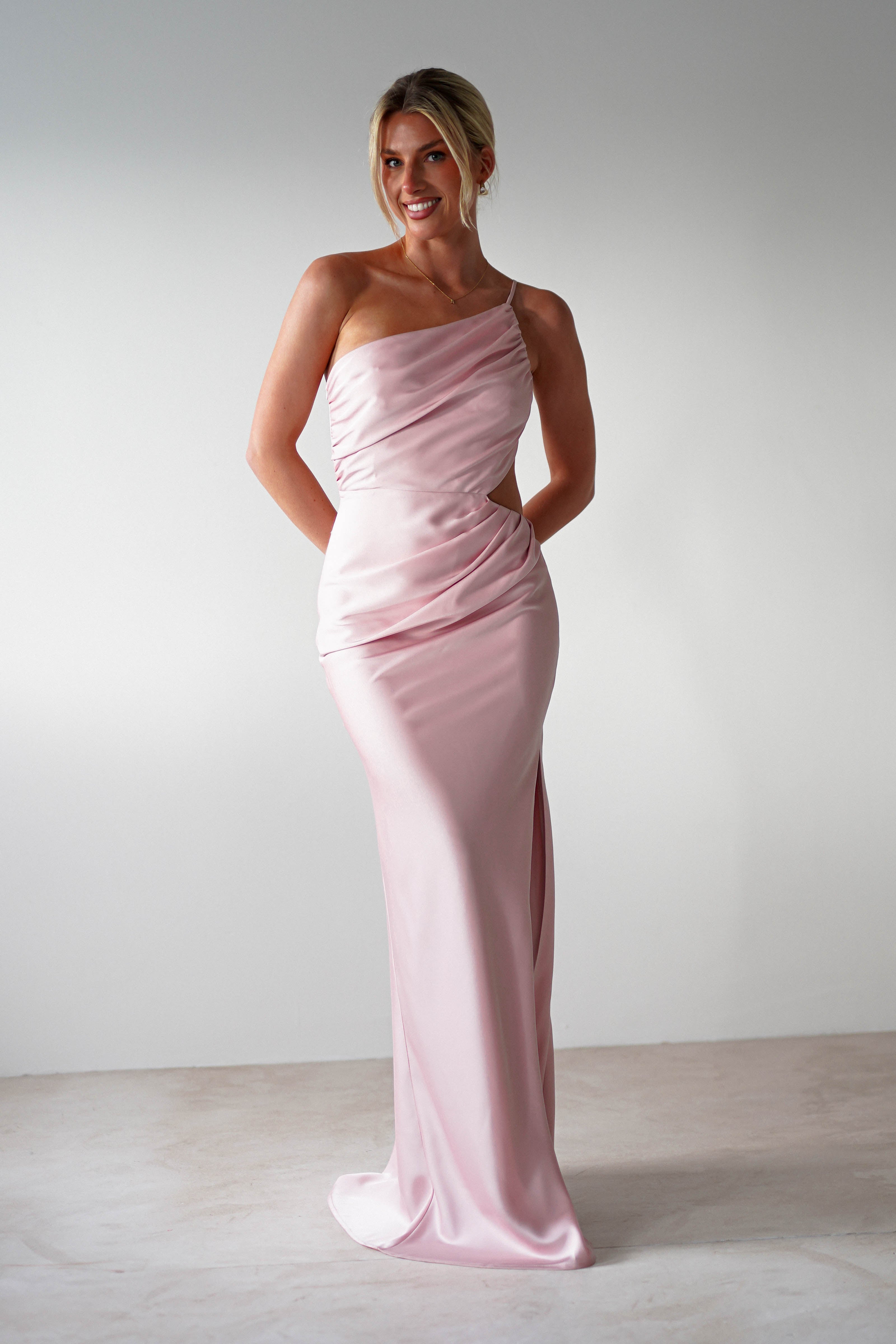 A woman in a pink satin maxi dress stands elegantly, perfect for a wedding guest dress.