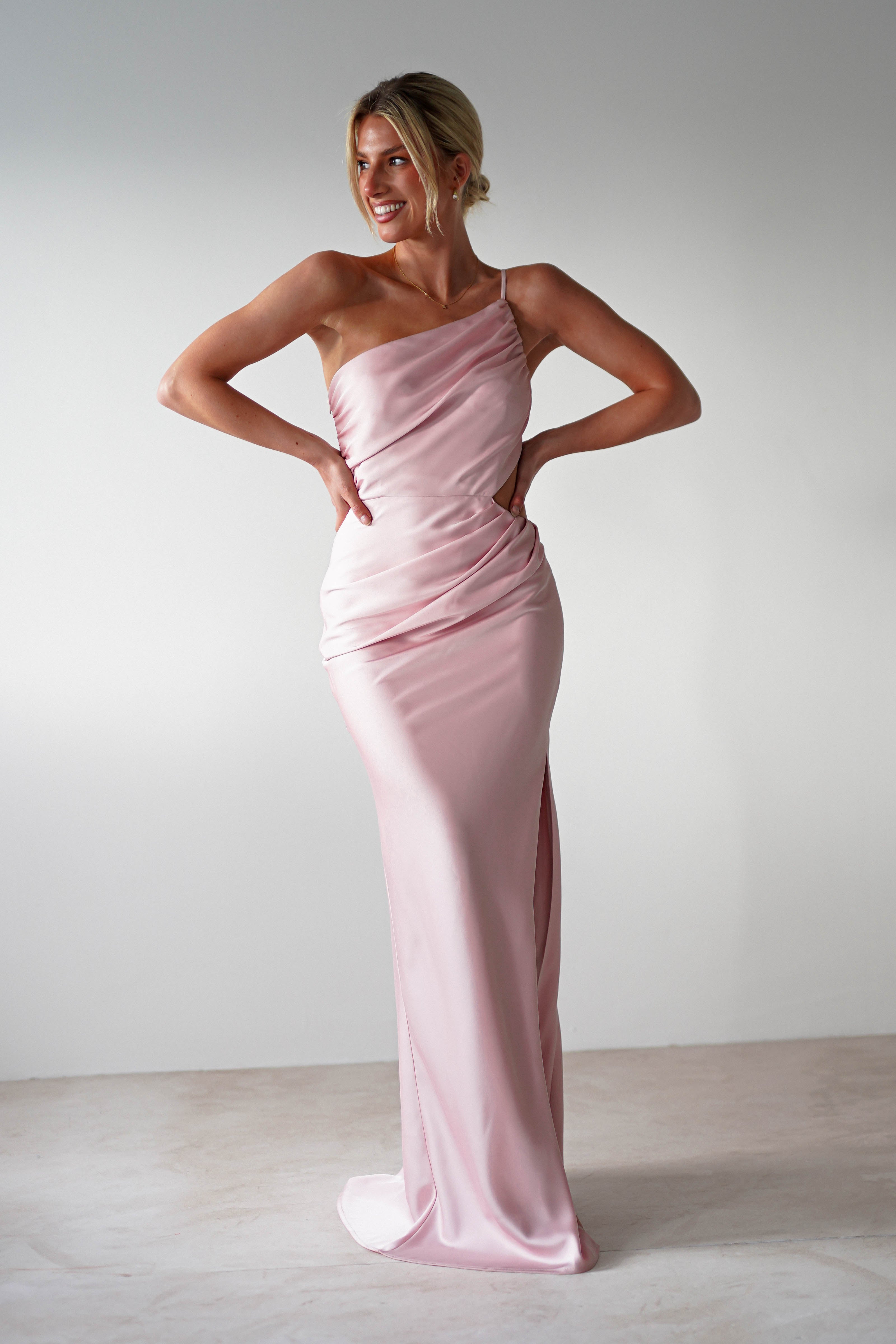 A woman in a pink one-shoulder satin maxi, perfect as a bridesmaids dress or for attending as a wedding guest.
