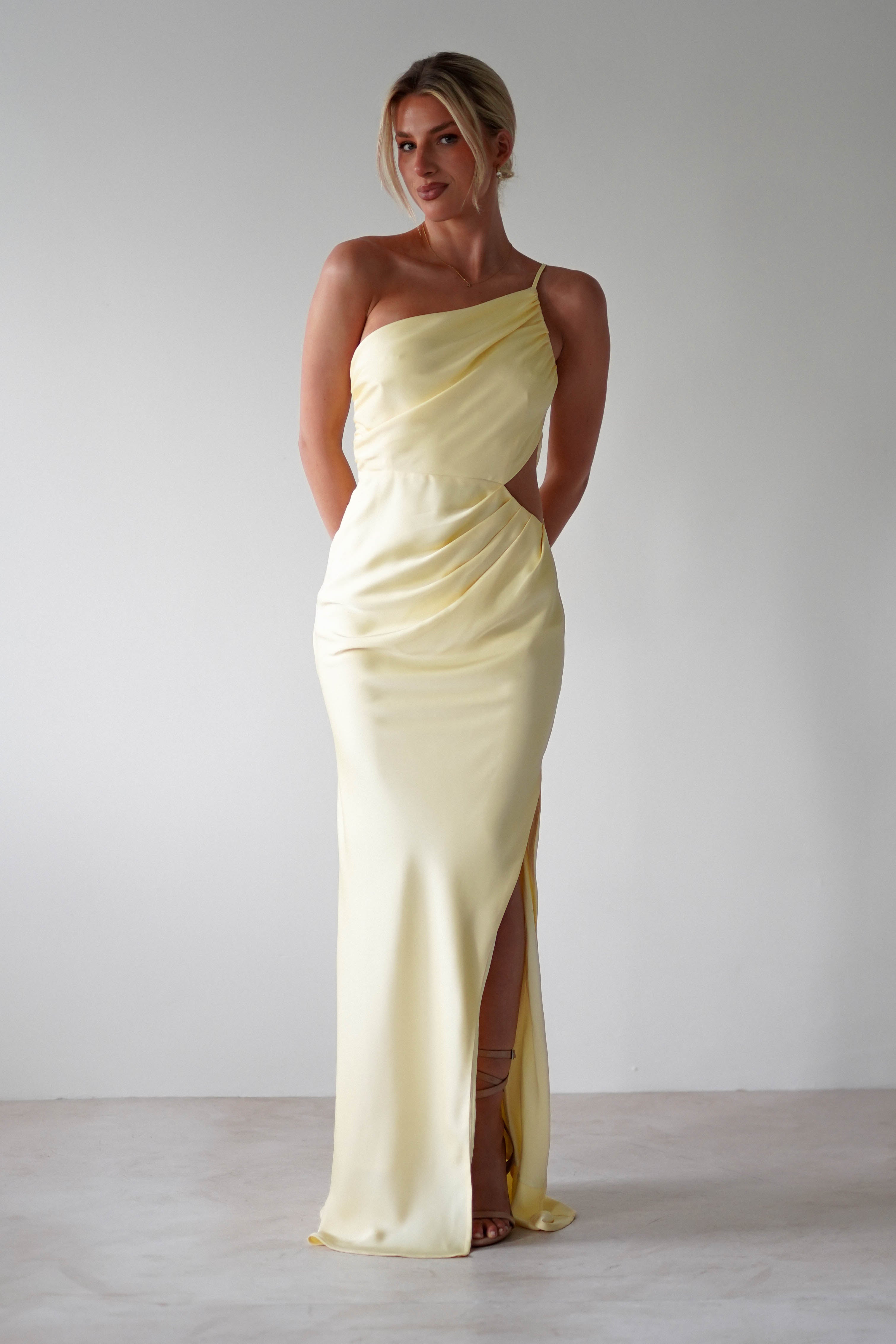 A woman in a matte satin yellow one-shoulder maxi dress.