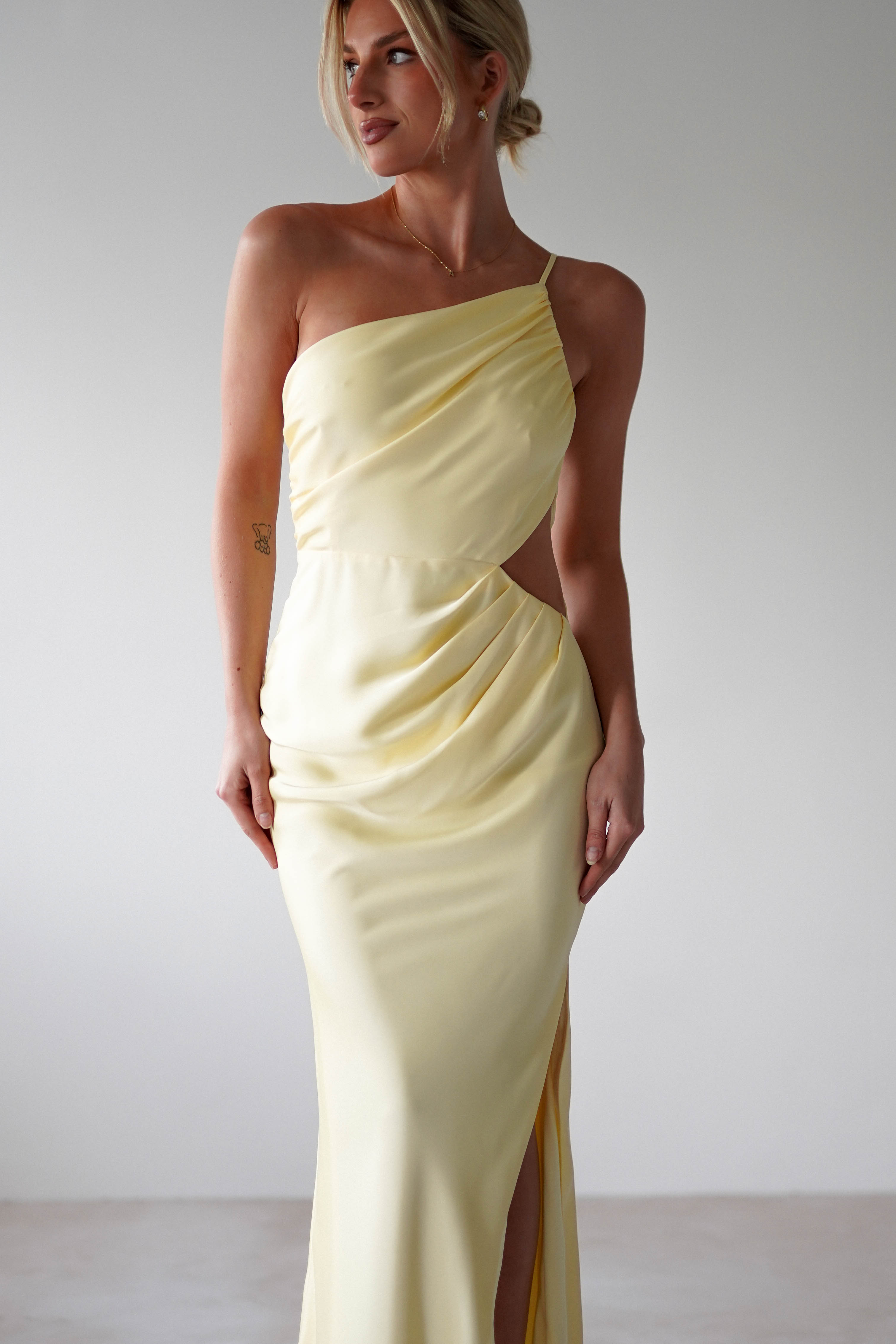 A woman in a matte satin yellow, one-shoulder satin maxi dress exudes elegance—perfect for bridesmaids.
