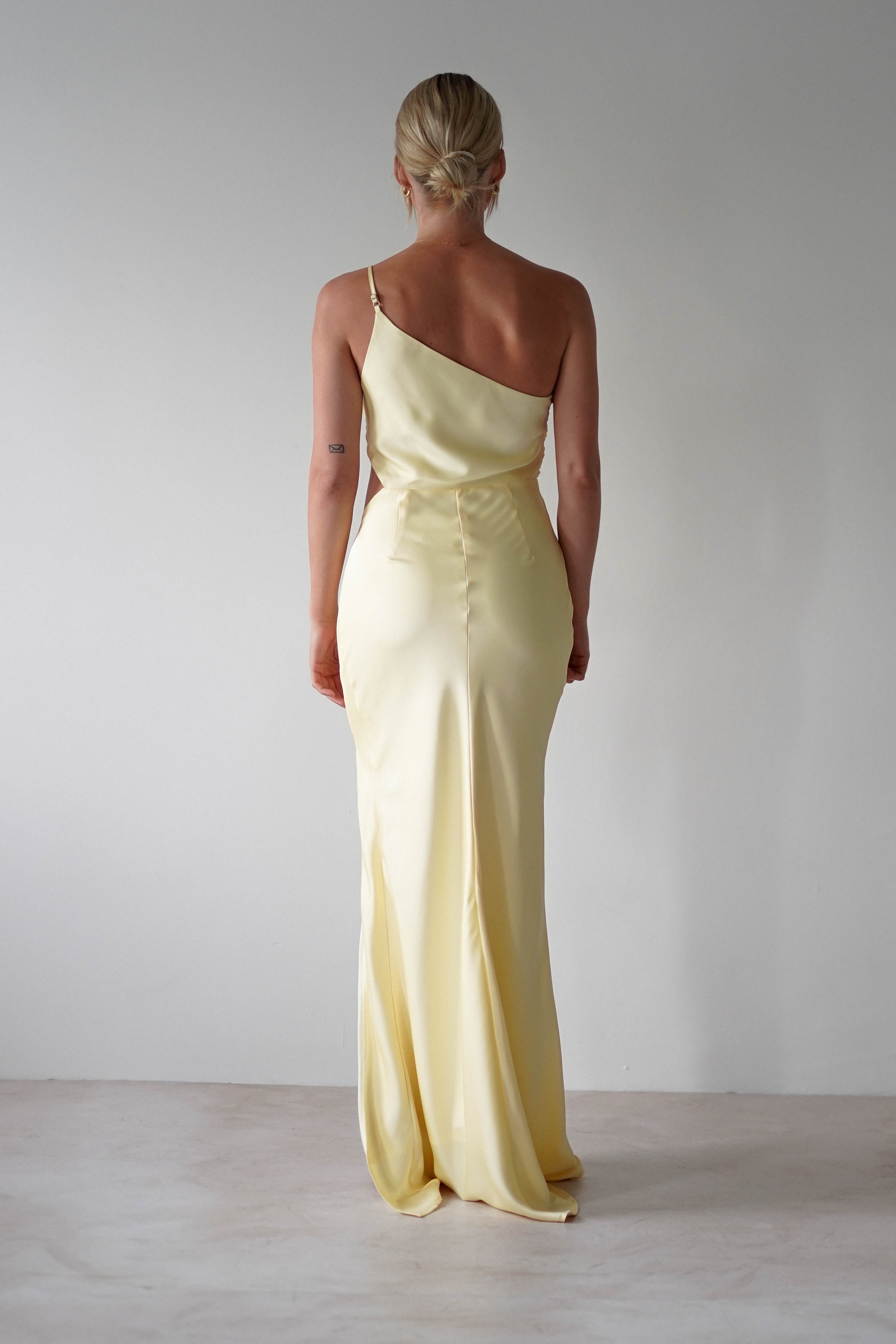A woman in a matte satin yellow one-shoulder maxi dress, perfect for bridesmaids.