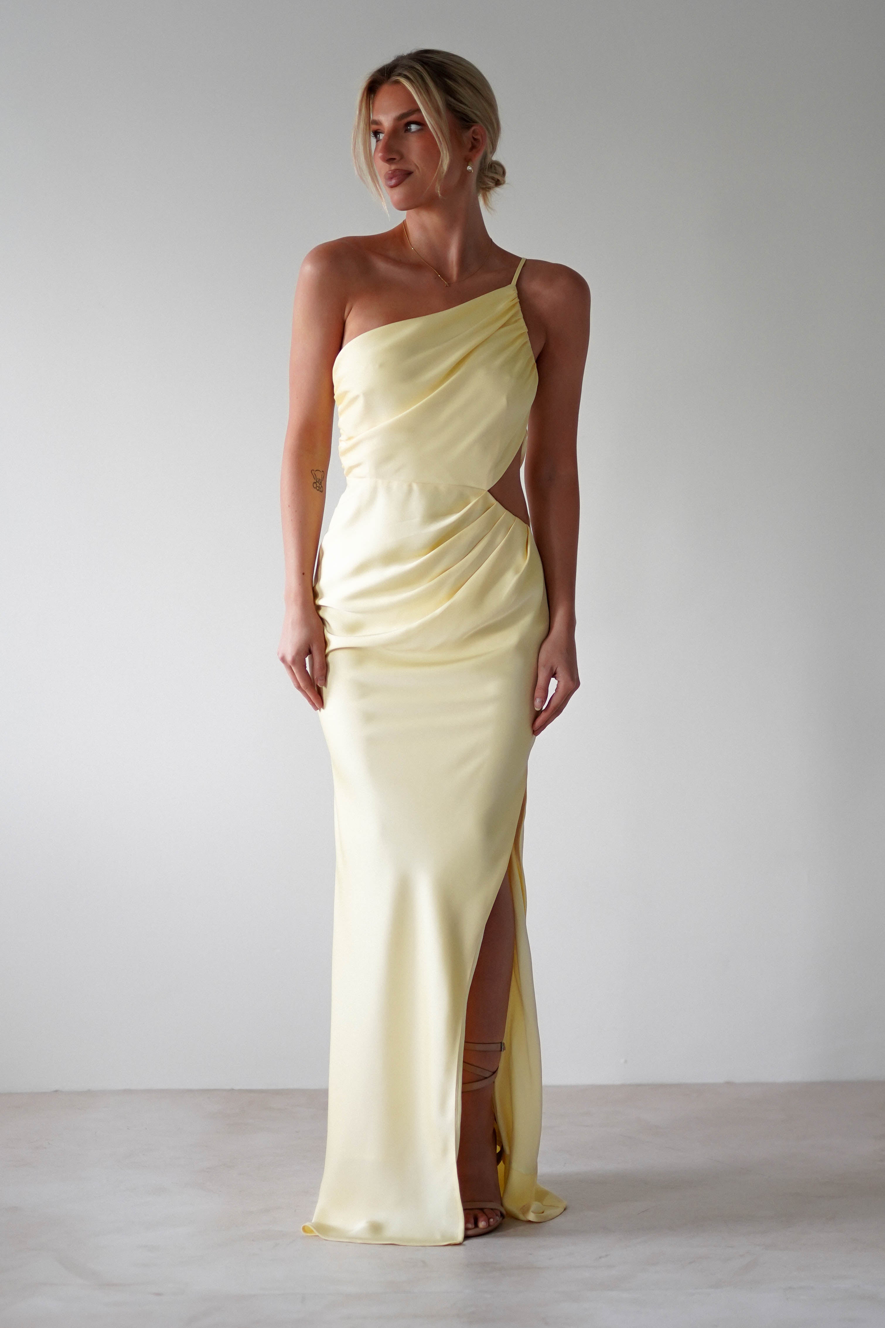 A woman in a matte satin yellow one-shoulder maxi dress, perfect for bridesmaids.