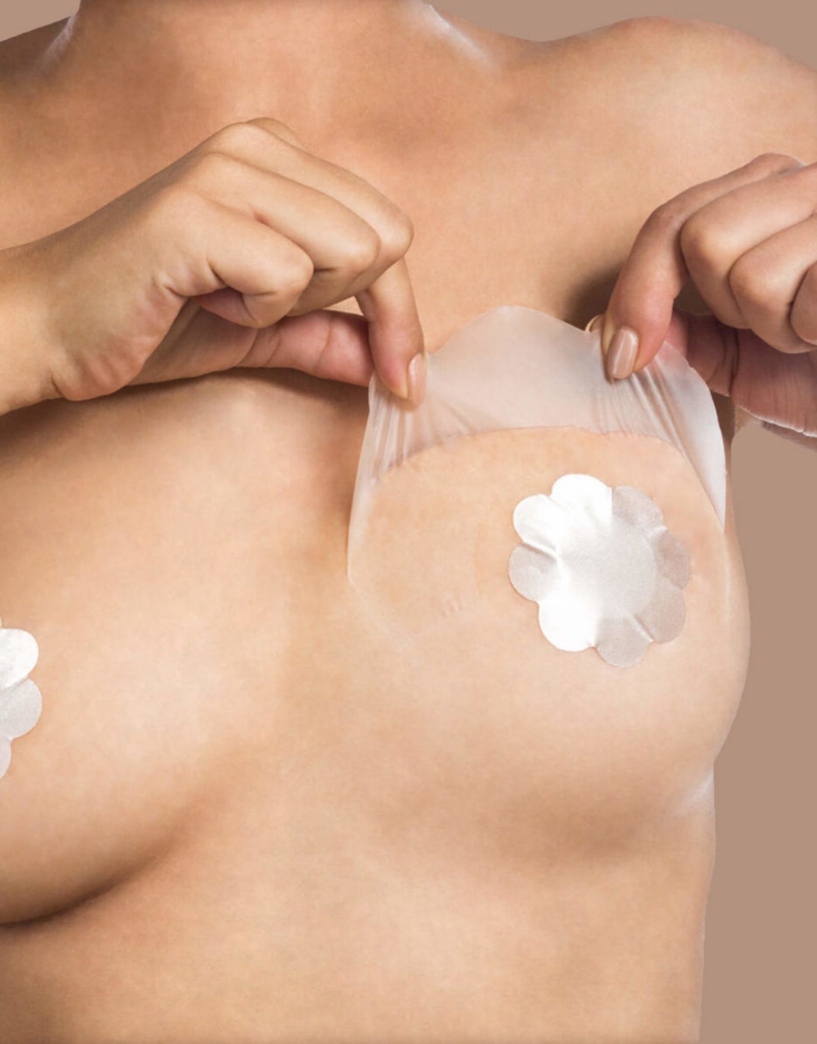 A person peeling off a clear adhesive layer over a flower-shaped Silk Nipple Cover on their chest. Their hands are pulling the adhesive away, revealing the smooth cover underneath. The neutral background highlights the elegance of this Bye Bra strapless solution.