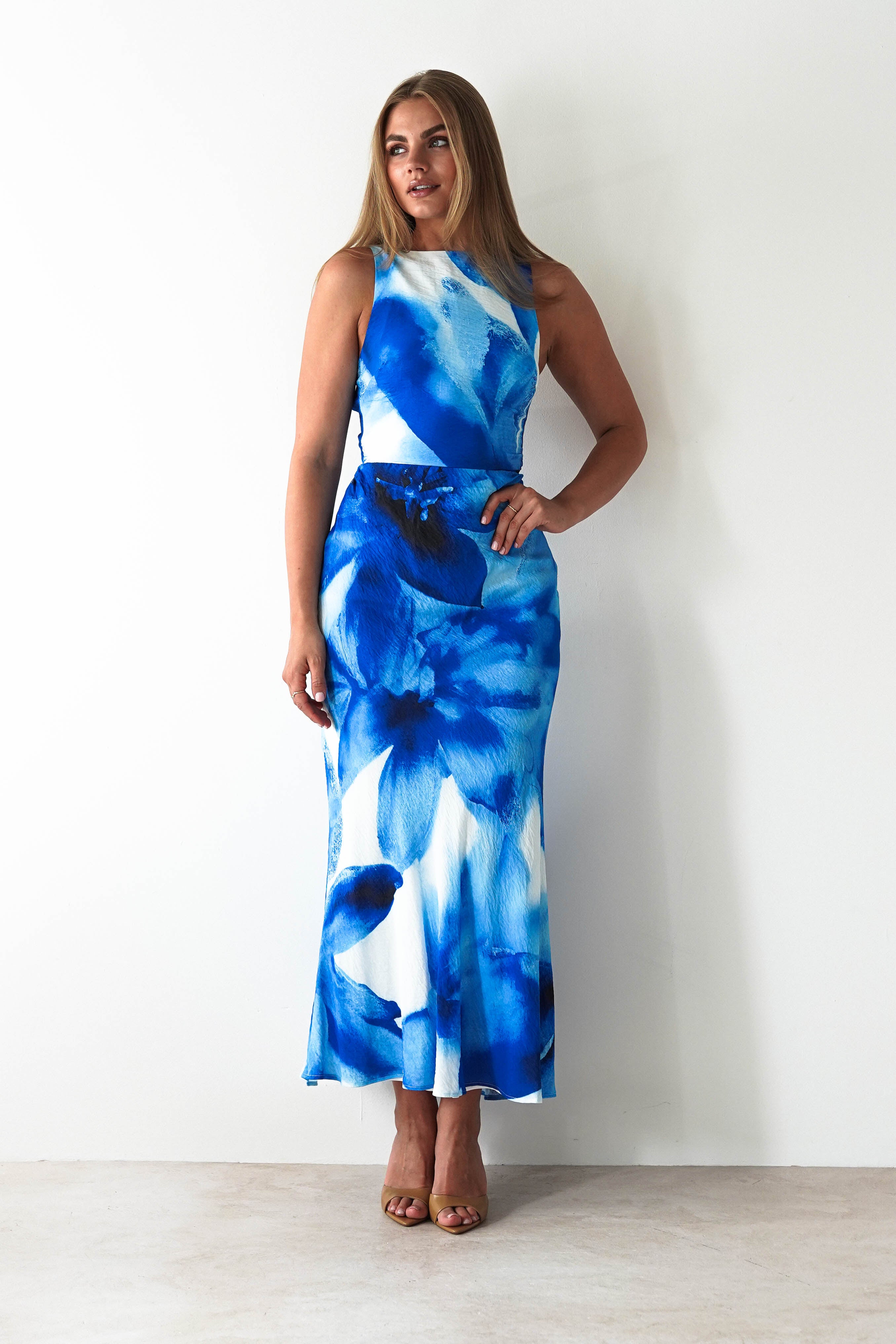 Blue floral maxi dress with ruffled shoulder straps, fitted bodice, and tiered flowing skirt, styled for elegant summer or special occasion wear.
