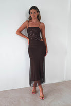 Woman wearing a brown sequin Angela maxi dress with sheer mesh overlay and thin straps, styled with nude heels against a neutral background.
