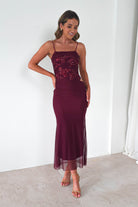 Woman wearing a wine sequin Angela maxi dress with sheer mesh skirt and thin straps, styled with nude heels against a light background.