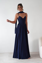 Woman wearing Felicity Lace Up Corset Maxi Dress in navy with thin straps, fitted corset bodice, and flowing full-length skirt, styled with a matching scarf.