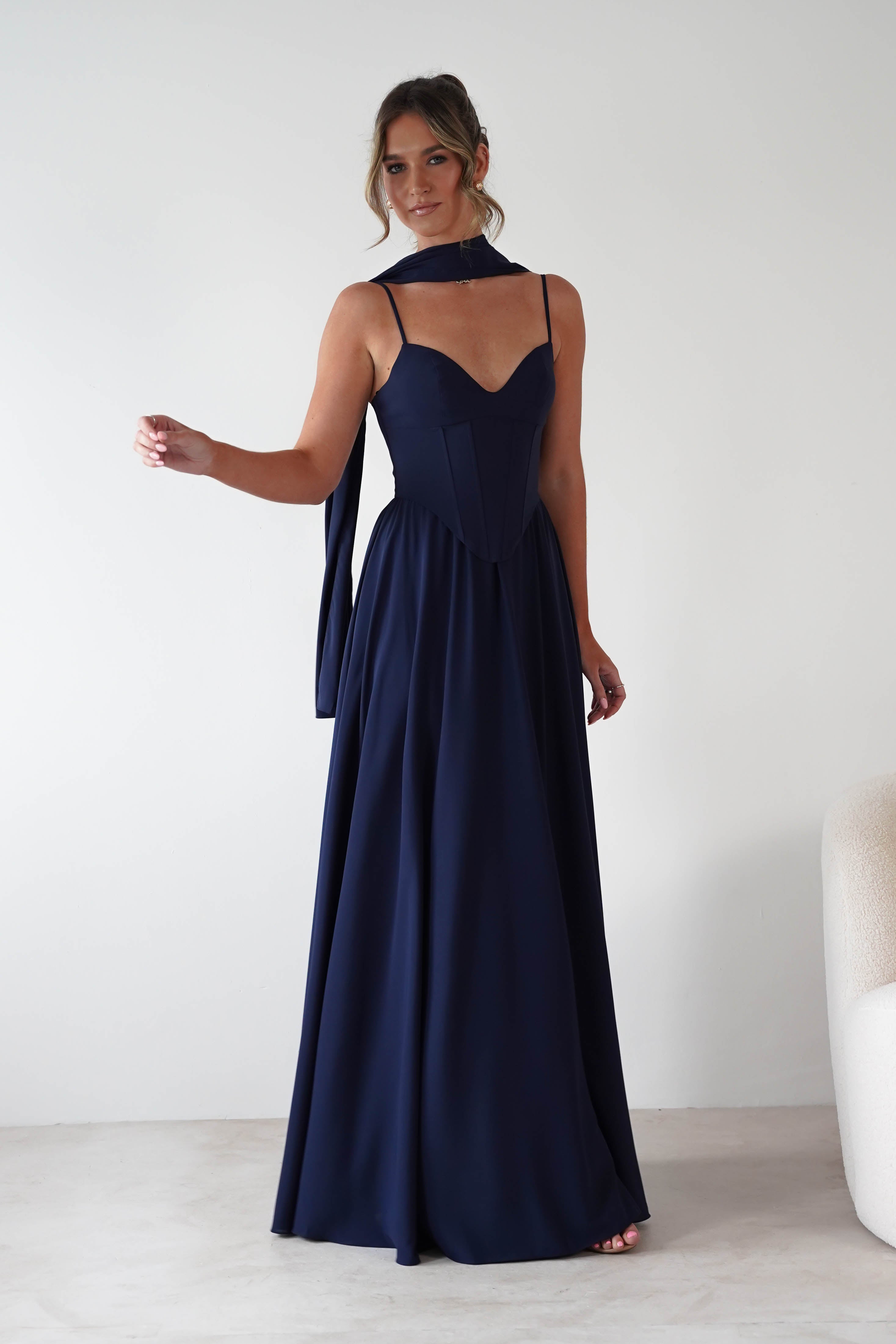 Woman wearing Felicity Lace Up Corset Maxi Dress in navy with thin straps, fitted corset bodice, and flowing full-length skirt, styled with a matching scarf.