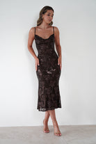 Woman wearing a brown sequin floral Jayna midi dress with cowl neckline and thin straps, styled with nude heels against a plain white background.