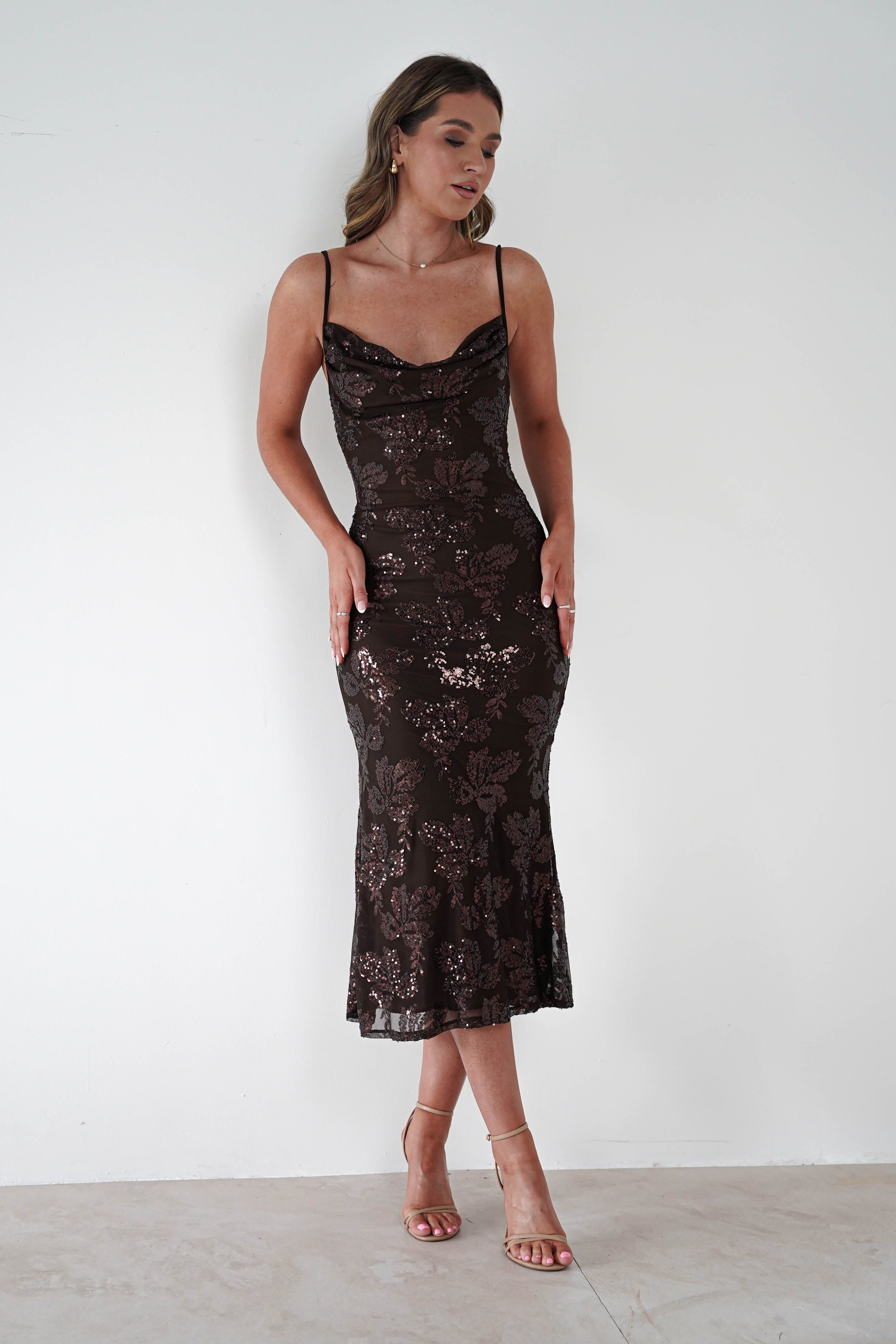 Woman wearing a brown sequin floral Jayna midi dress with cowl neckline and thin straps, styled with nude heels against a plain white background.