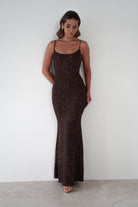 Woman wearing a brown sequin Maria bodycon maxi gown with thin straps and fitted silhouette, styled with nude heels against a plain white background.