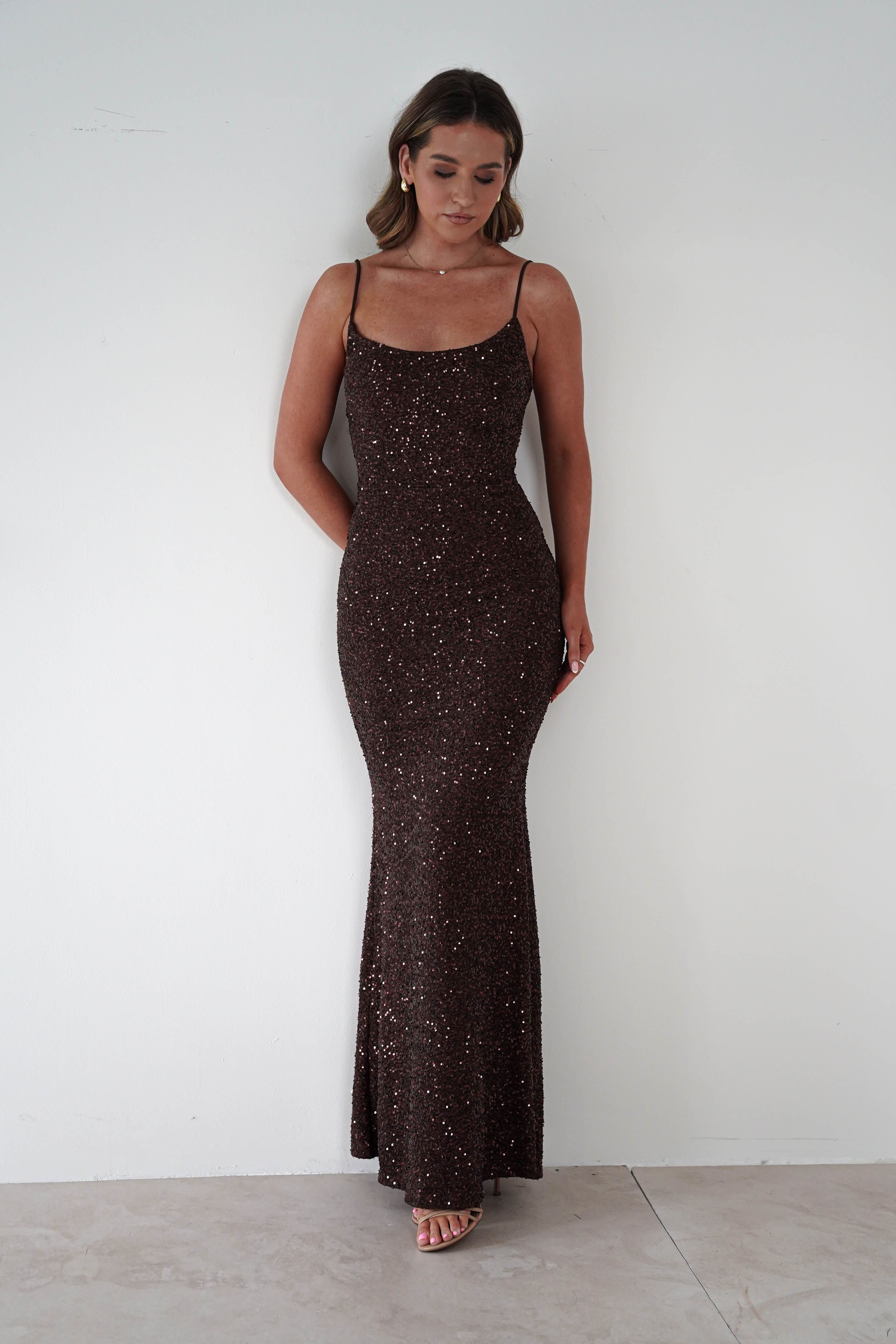 Woman wearing a brown sequin Maria bodycon maxi gown with thin straps and fitted silhouette, styled with nude heels against a plain white background.