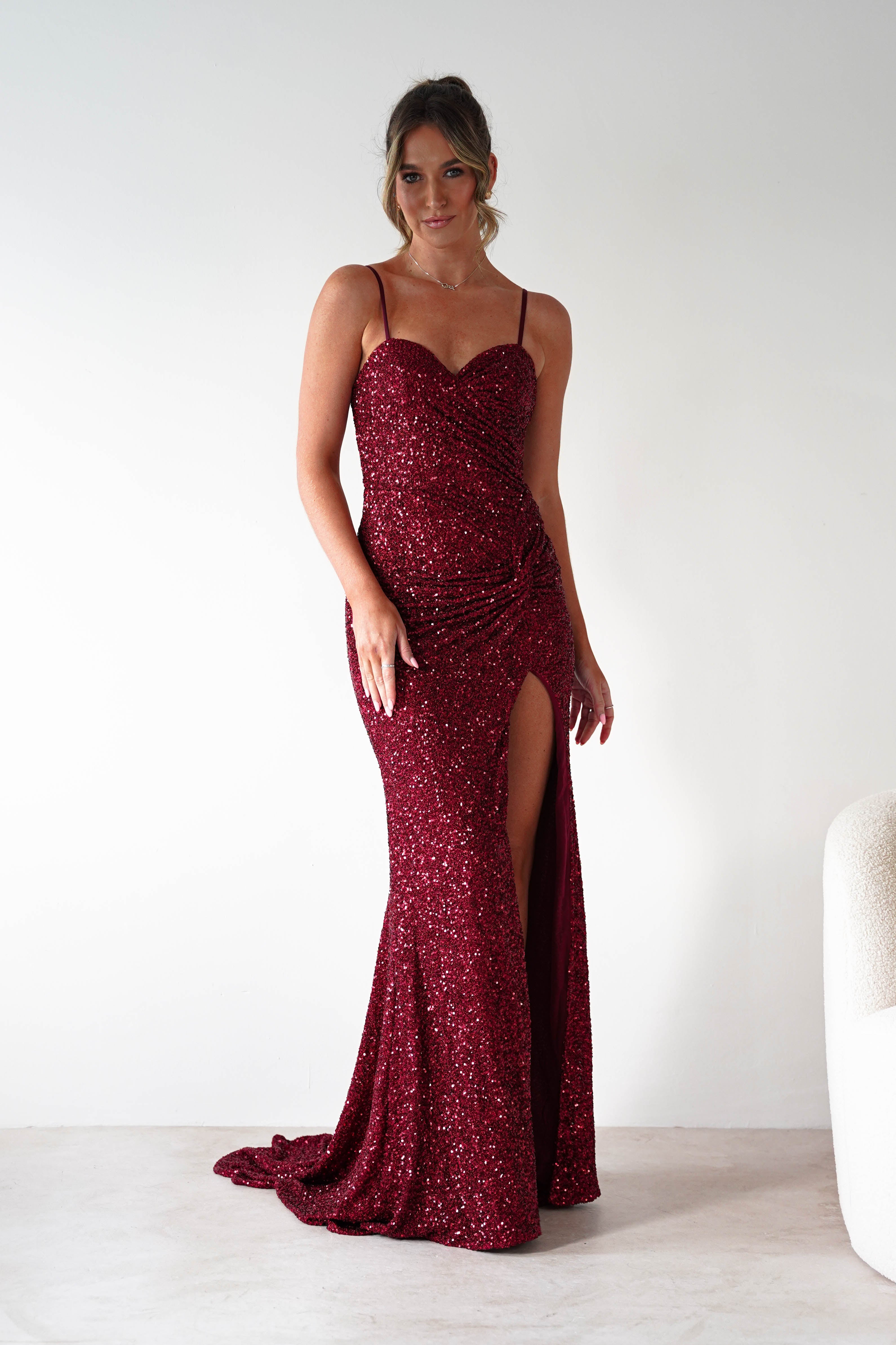 Woman wearing Nalita Bodycon Sequin Gown in deep red with sweetheart neckline, fitted silhouette, sparkling sequin finish, and high leg slit.