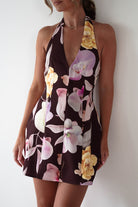 Woman wearing Peony Structured Halter Neck Mini Dress in brown with a plunging neckline, bold pink and yellow floral print, and a fitted, tailored silhouette.