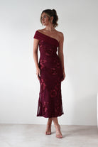 Woman wearing Rochelle Off The Shoulder Midi Dress in wine with floral embroidery, fitted silhouette, and asymmetrical draped neckline, styled with nude heels.