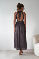 Woman wearing Sivana Polka Dot Skater Maxi Dress in brown with white polka dots, halter tie-back neckline, open back, and flowy maxi skirt styled with nude heels.