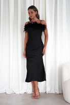 Woman wearing a black dress with feather details against a white curtain background