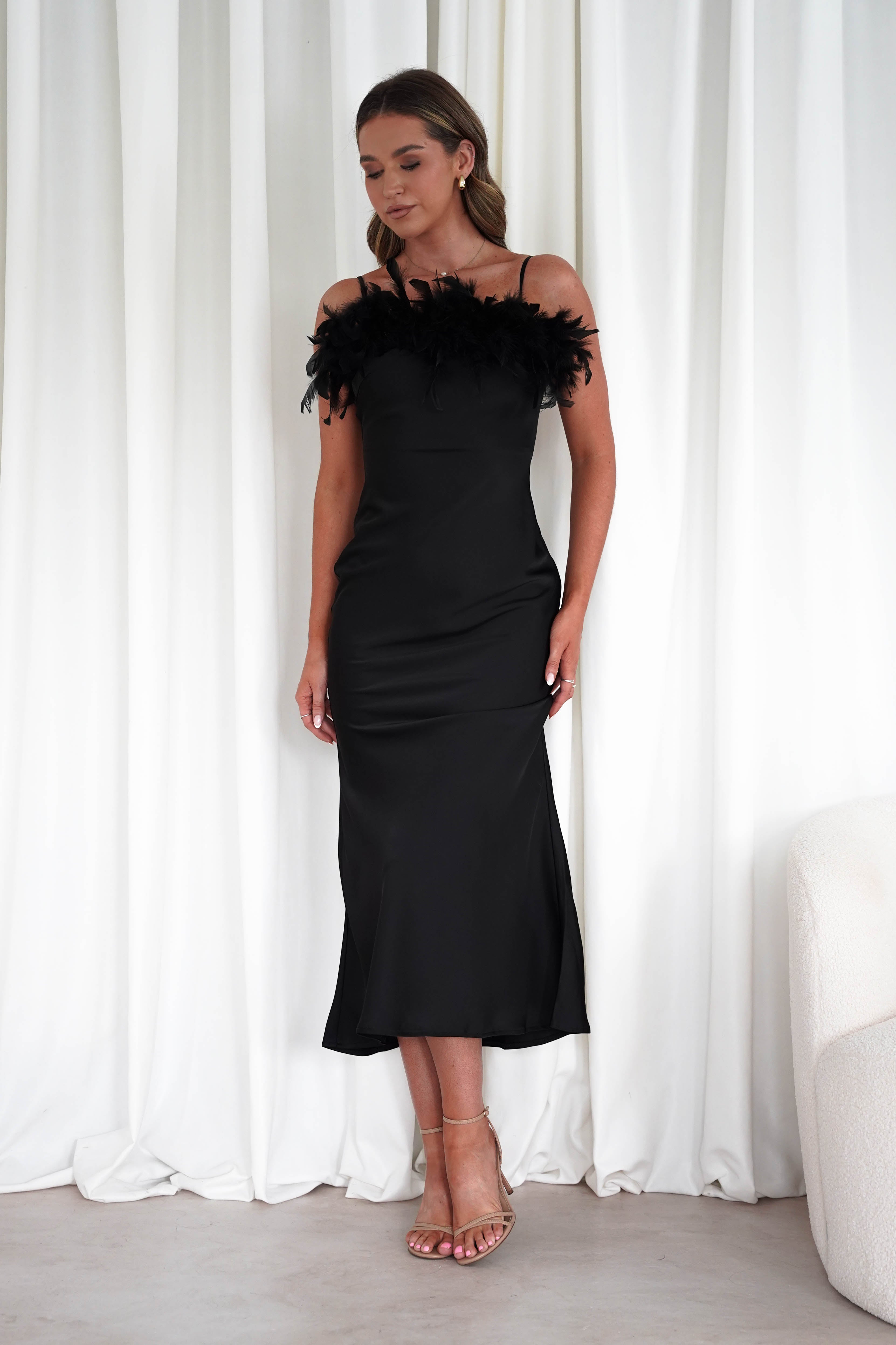 Woman wearing a black dress with feather details against a white curtain background